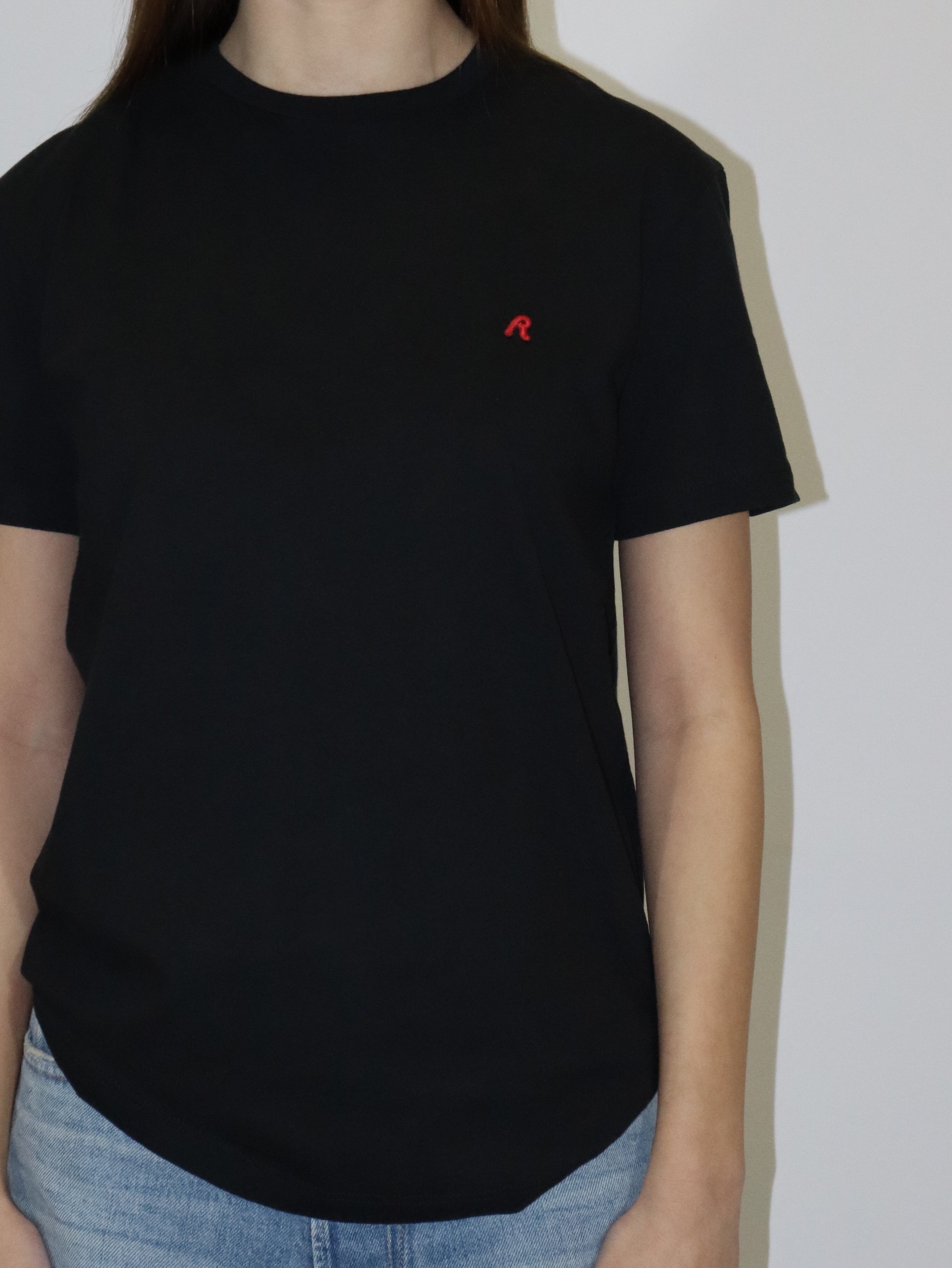 Dámské černé tričko Replay s krátkým rukávem a malým červeným logem, světlé volné džíny, postava proti bílému pozadí.