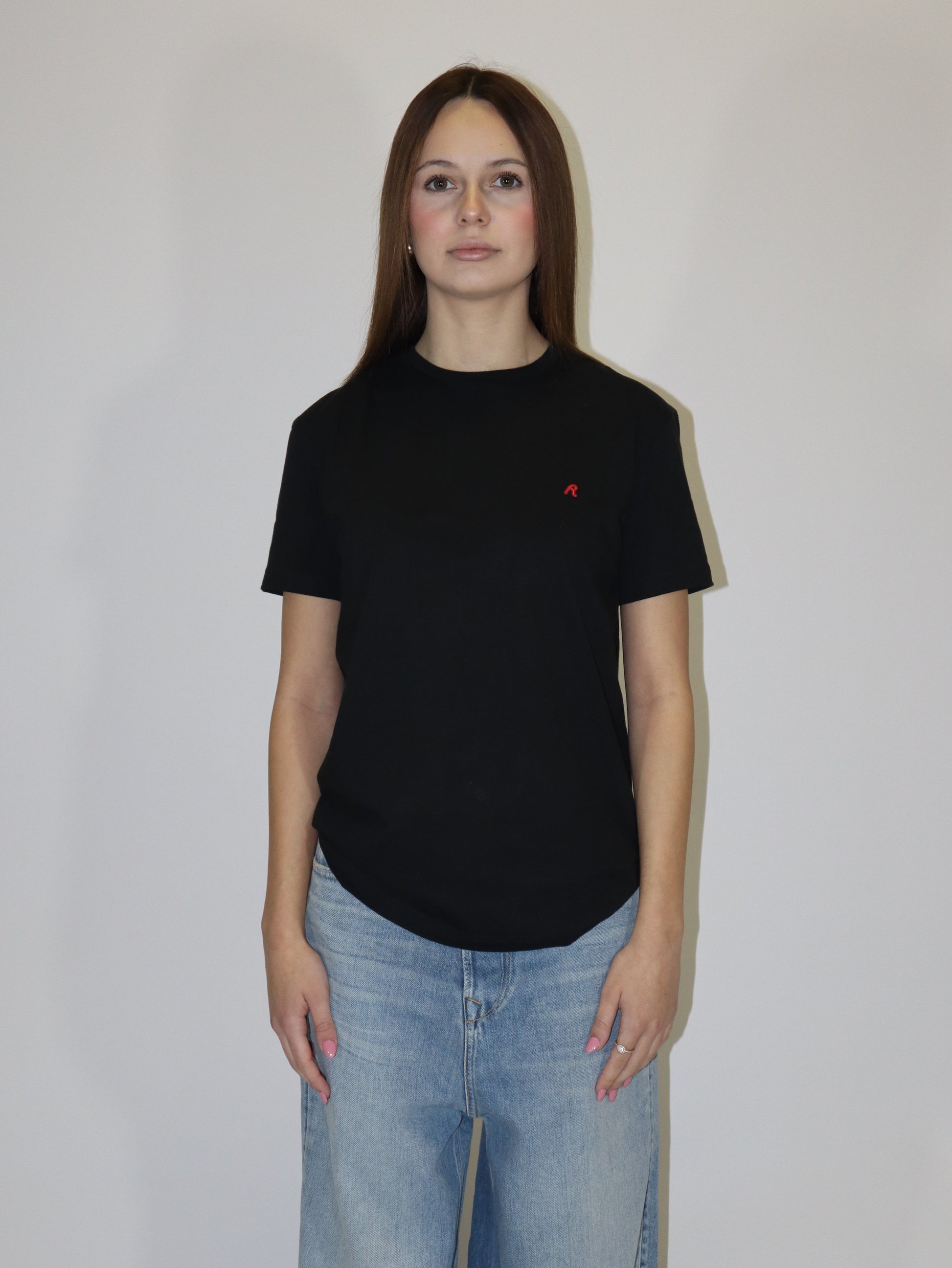 Dámské černé tričko Replay s krátkým rukávem a malým červeným logem, světlé volné džíny, postava proti bílému pozadí.