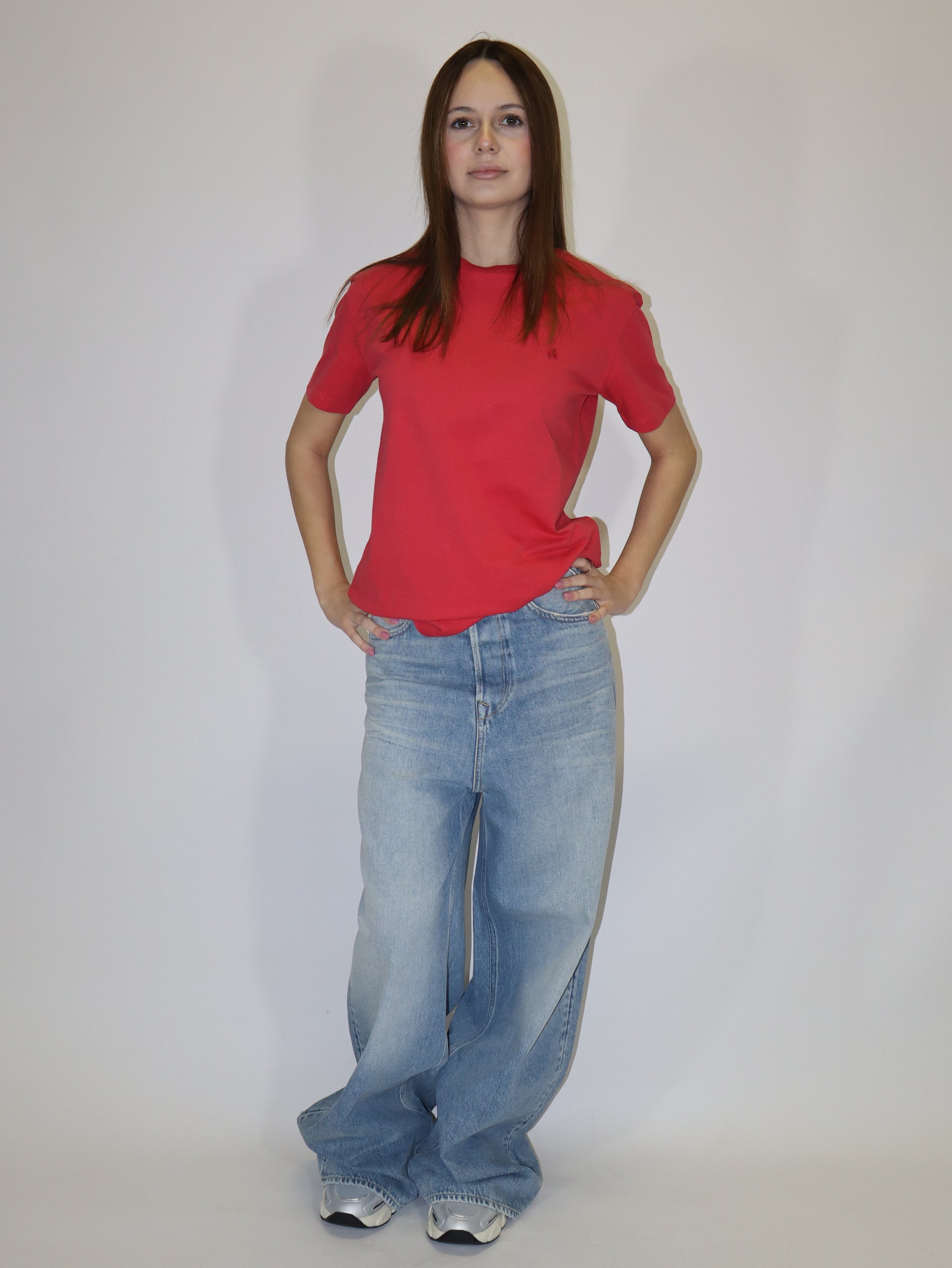 Dámské červené tričko Replay s krátkým rukávem a malým červeným logem, světlé volné džíny, postava proti bílému pozadí.