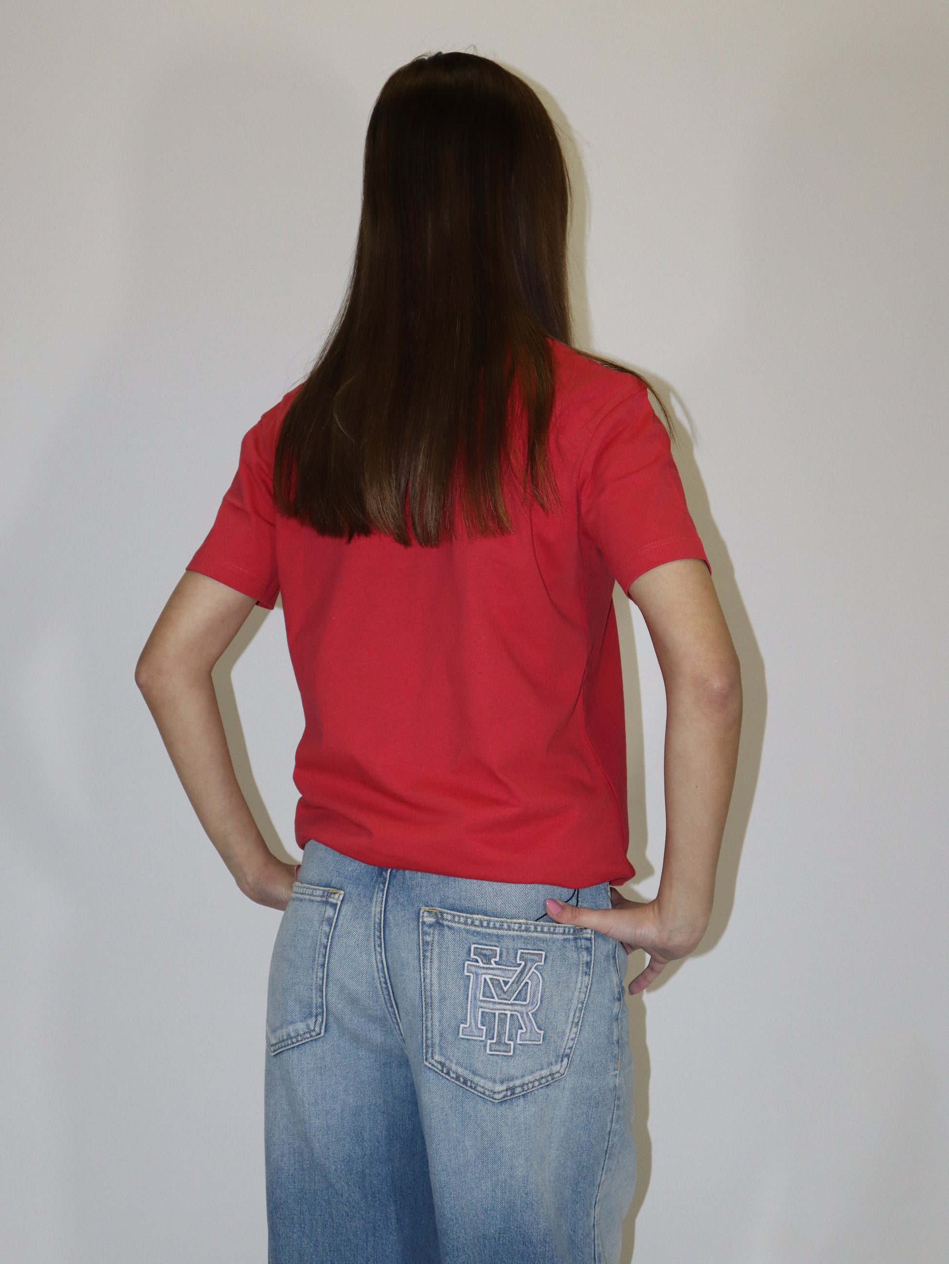 Dámské červené tričko Replay s krátkým rukávem a malým červeným logem, světlé volné džíny, postava proti bílému pozadí.
