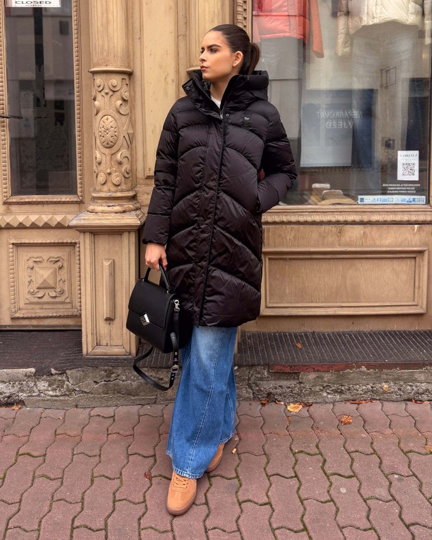 Dámský dlouhý kabát BLAUER Opera s šikmým prošíváním černý - modelka v modrých džínách, přední pohled